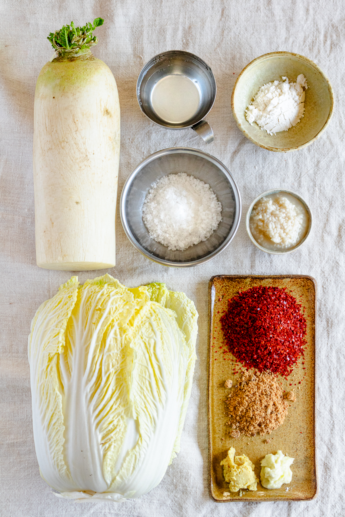 Ingredients for vegan kimchi: daikon, napa cabbage, salt, water, rice flour, shio koji, gochugaru, black sugar, garlic, and ginger