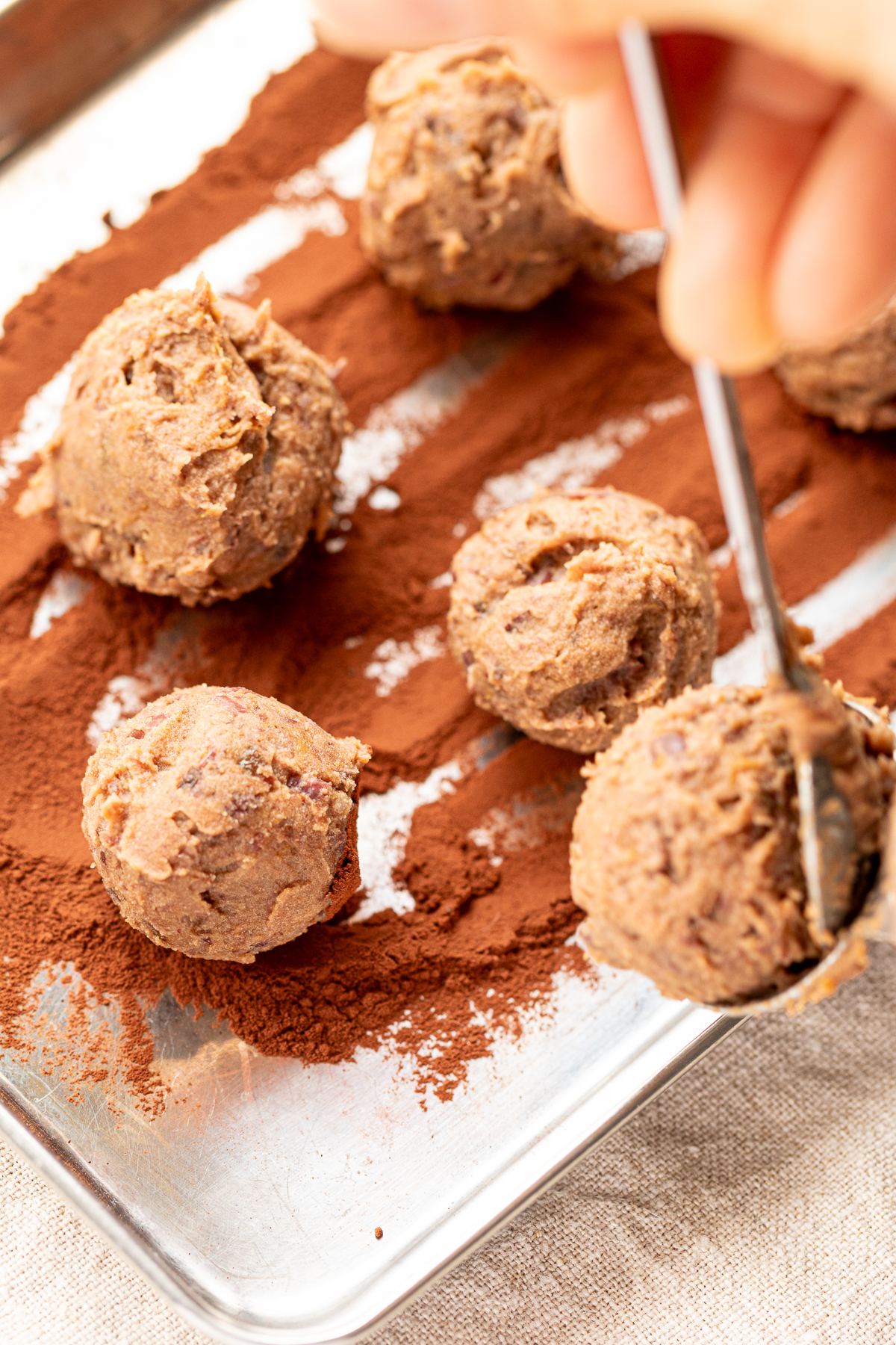 Dropping shaped vegan Nama chocolate truffle onto a tray dusted with cocoa powder