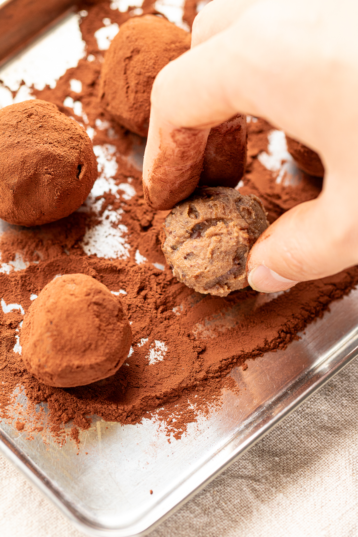 Rolling vegan chocolate truffles in cocoa powder on a tray