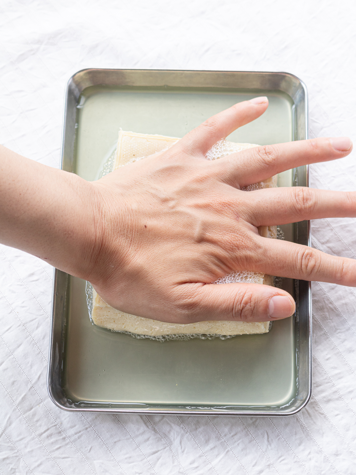 Frozen cotton (momen) tofu is being squeezed by applying weight from above with the palm of the hand.
