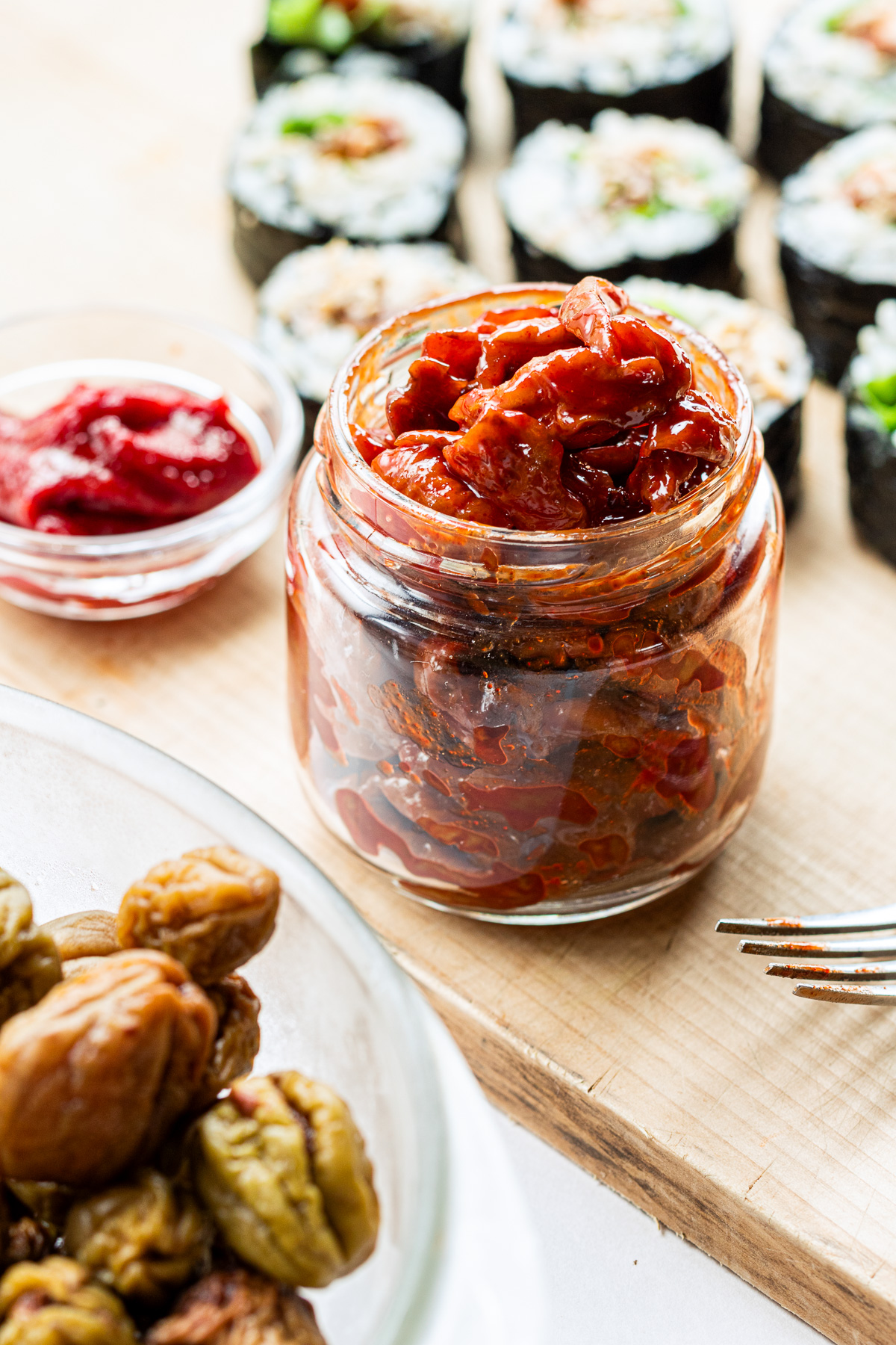 Maesil jangajji in a glass jar with homemade vegan kimbap using pickled plums