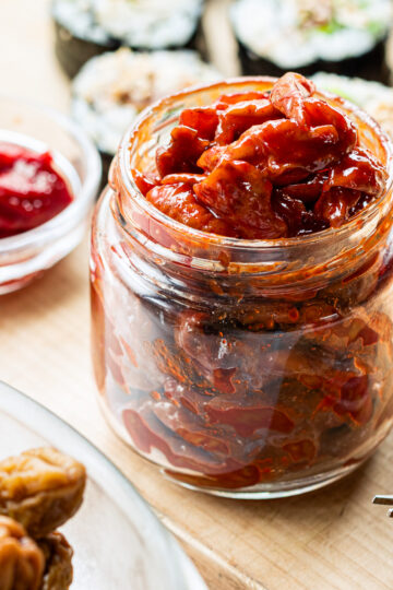 Maesil jangajji in a glass jar with homemade vegan kimbap using pickled plums