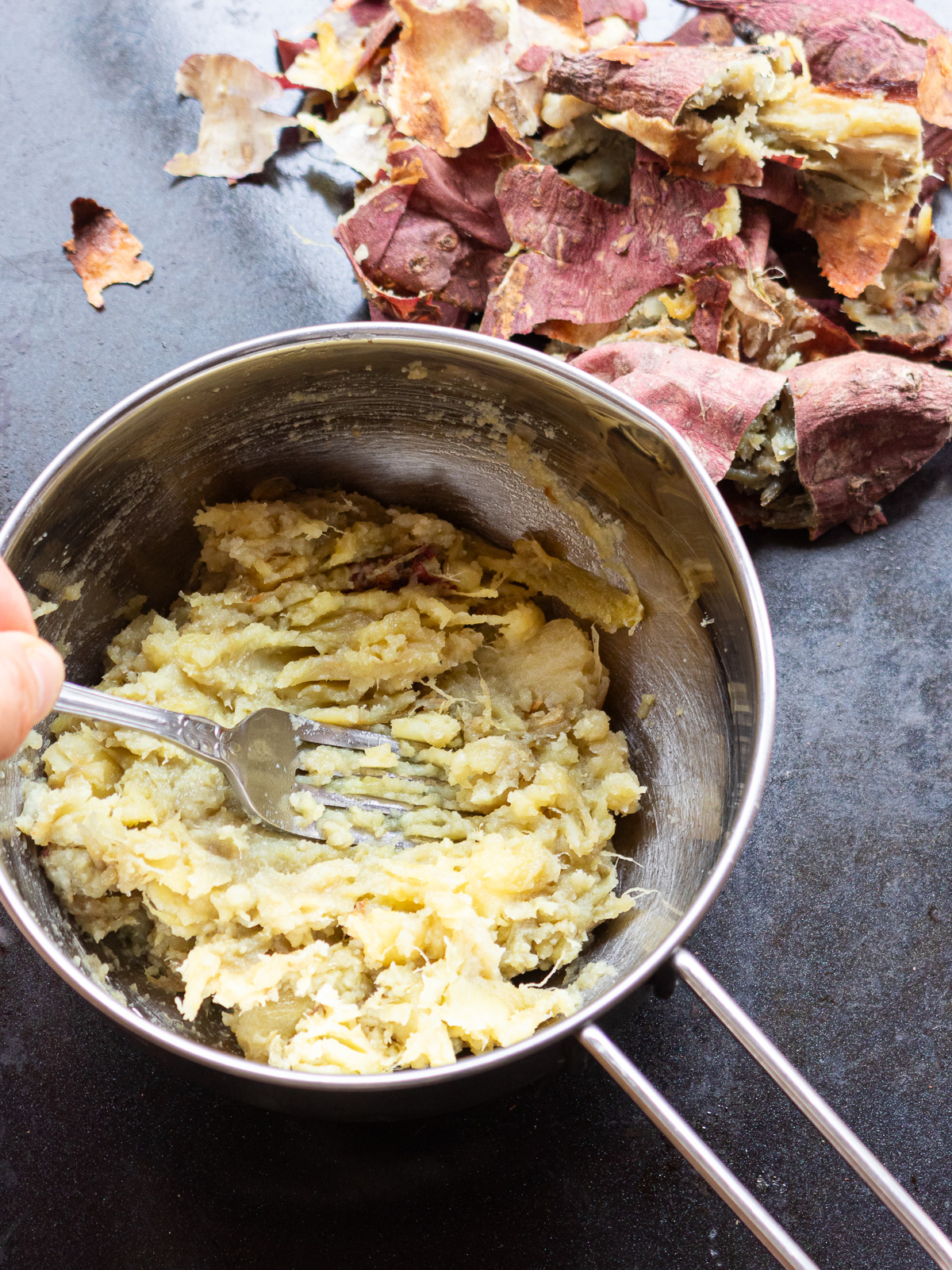 Peeled baked sweet potato mashed with fork in bowl for vegan bliss balls
