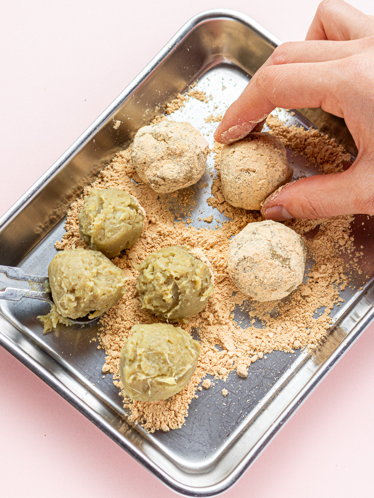 Rolled sweet potato balls being coated in kinako on tray