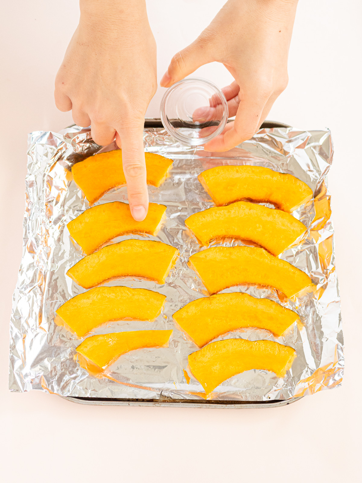 Rubbing oil on sliced kabocha arranged on foil-lined baking sheet