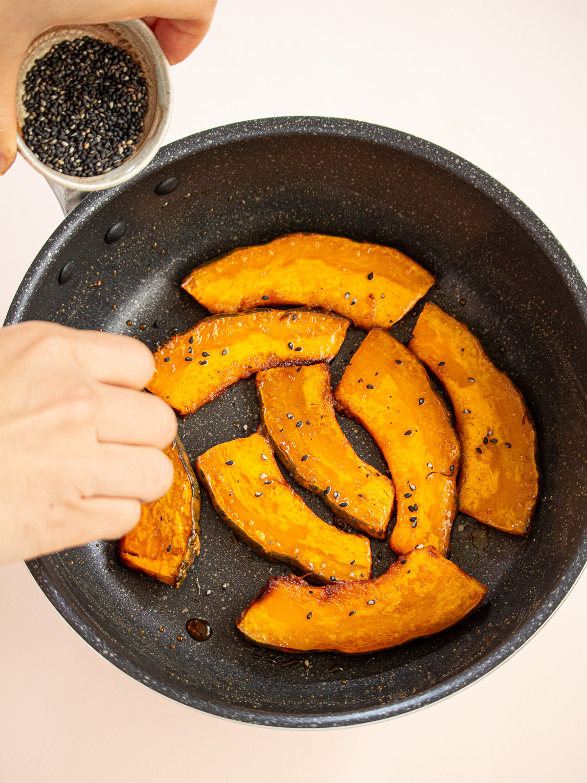 Coating baked kabocha with thickened maple glaze and black sesame seeds in frying pan