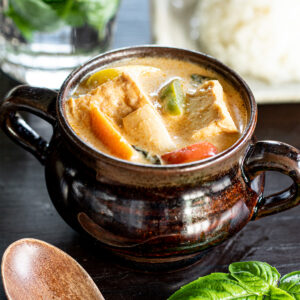 Creamy vegan red curry made without curry paste, showing colorful paprika, eringi mushrooms, and golden cubes of atsuage in coconut-based broth, served with rice.