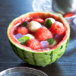 Vegan summer dessert: watermelon fruit punch served in a carved watermelon, topped with chewy banana mochi, pink agar jelly, and fresh mint.