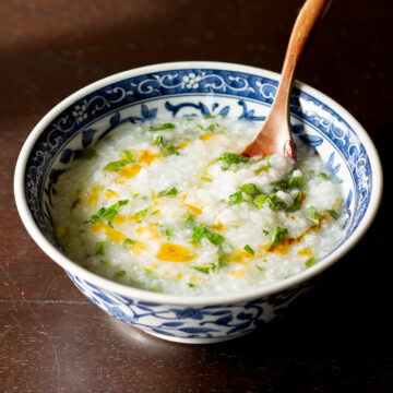 Vegan Asian breakfast congee in blue bowl with radish greens, turnip greens, cilantro and chili oil drizzle
