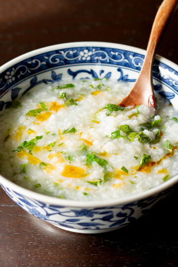 Vegan Asian breakfast congee in blue bowl with radish greens, turnip greens, cilantro and chili oil drizzle