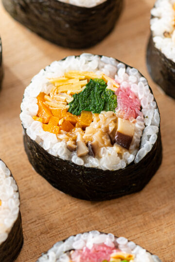 Vegan futomaki sushi roll with plant-based fillings including mushroom soboro, butternut squash kinpira, vegan kinshi tamago, spinach, and pickled onion