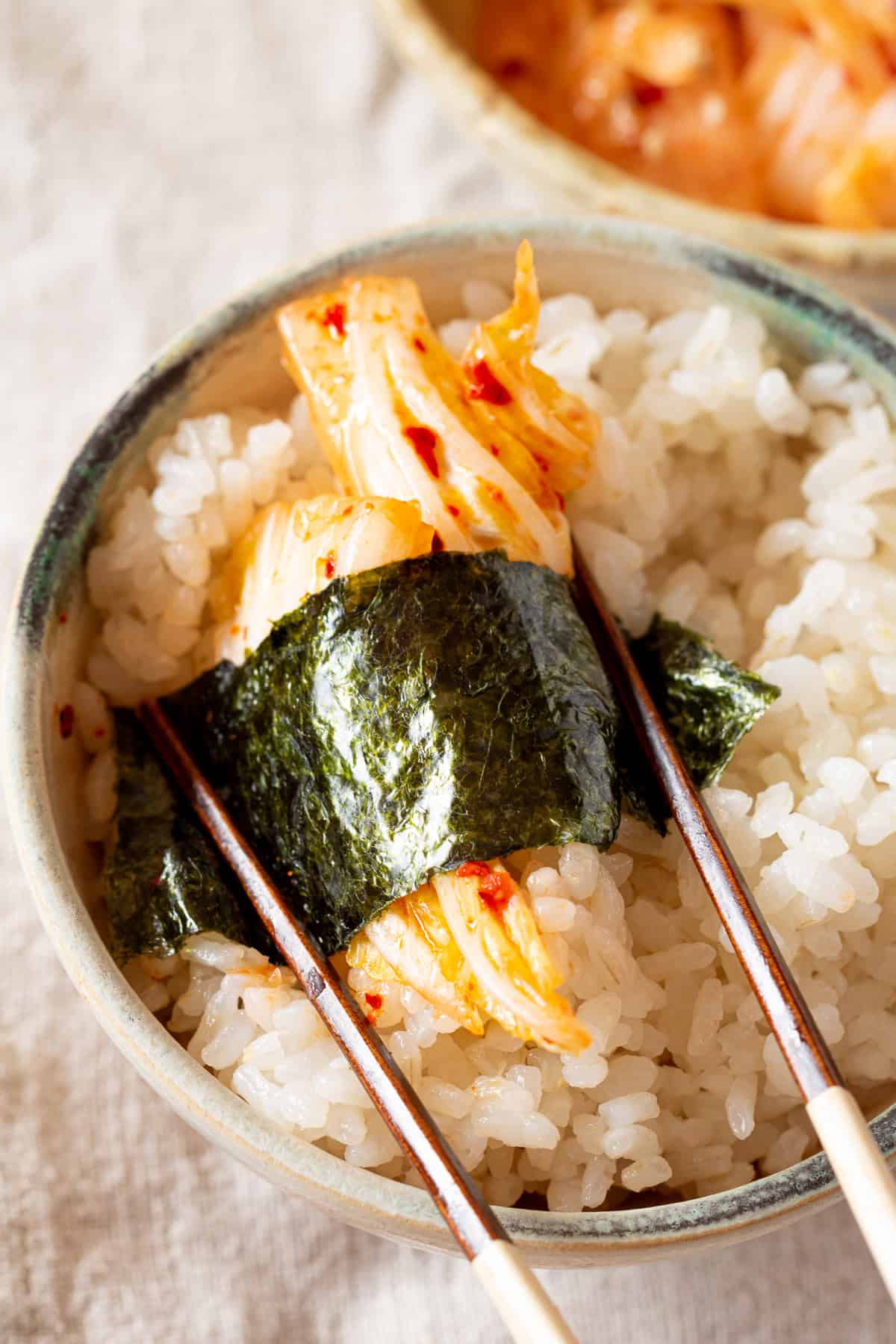 白米とヴィーガン旨辛白菜あえを箸を使って海苔で巻く