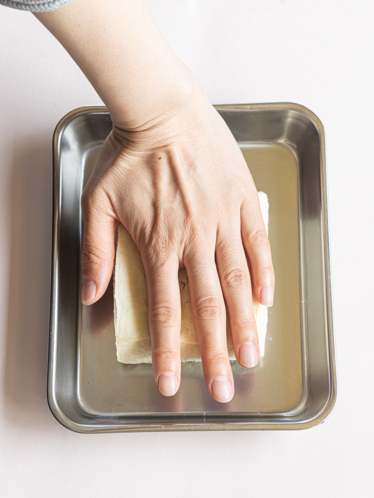 Squeeze out the water by pressing the thawed frozen tofu placed on the cooking tray from above with the palm of your hand.