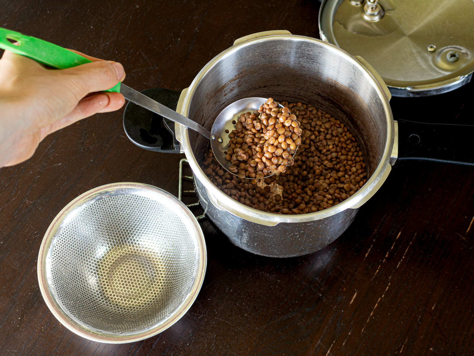 圧力鍋で茹で上げた皮付きレンズ豆をおたまですくっているところ
