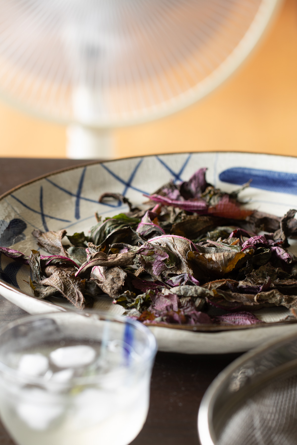 Red shiso leaves drying in front of a fan, accompanied by homemade ume chai syrup. A peaceful summer kitchen moment.