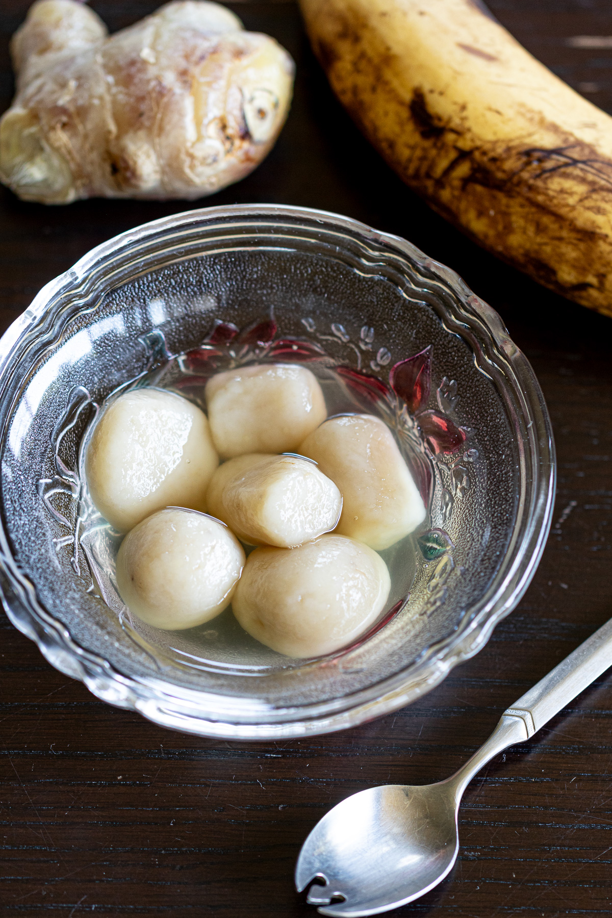 Japanese summer dessert — banana shiratama dumplings topped with ginger syrup, styled with whole bananas and fresh ginger roots.
