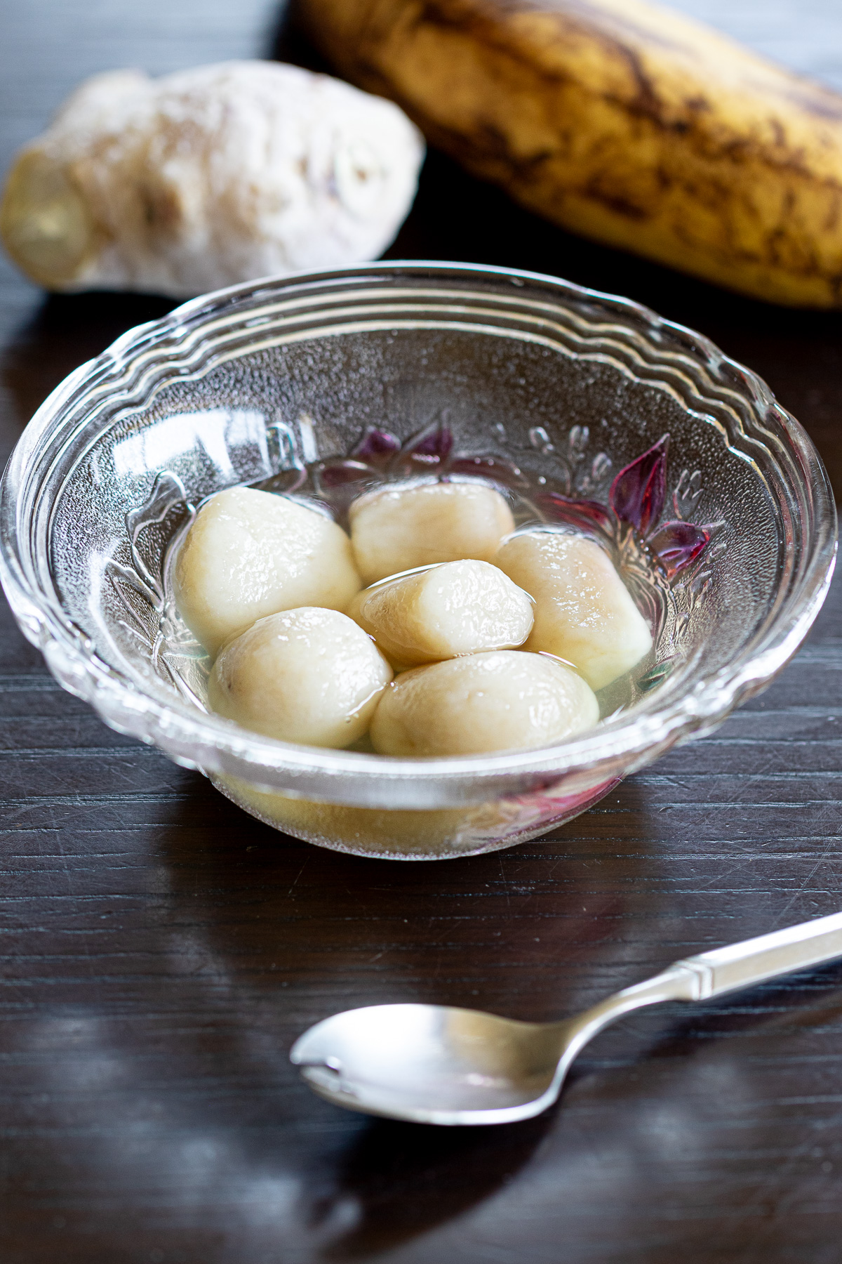 Vegan banana shiratama dumplings in ginger syrup with fresh banana and ginger in the background.