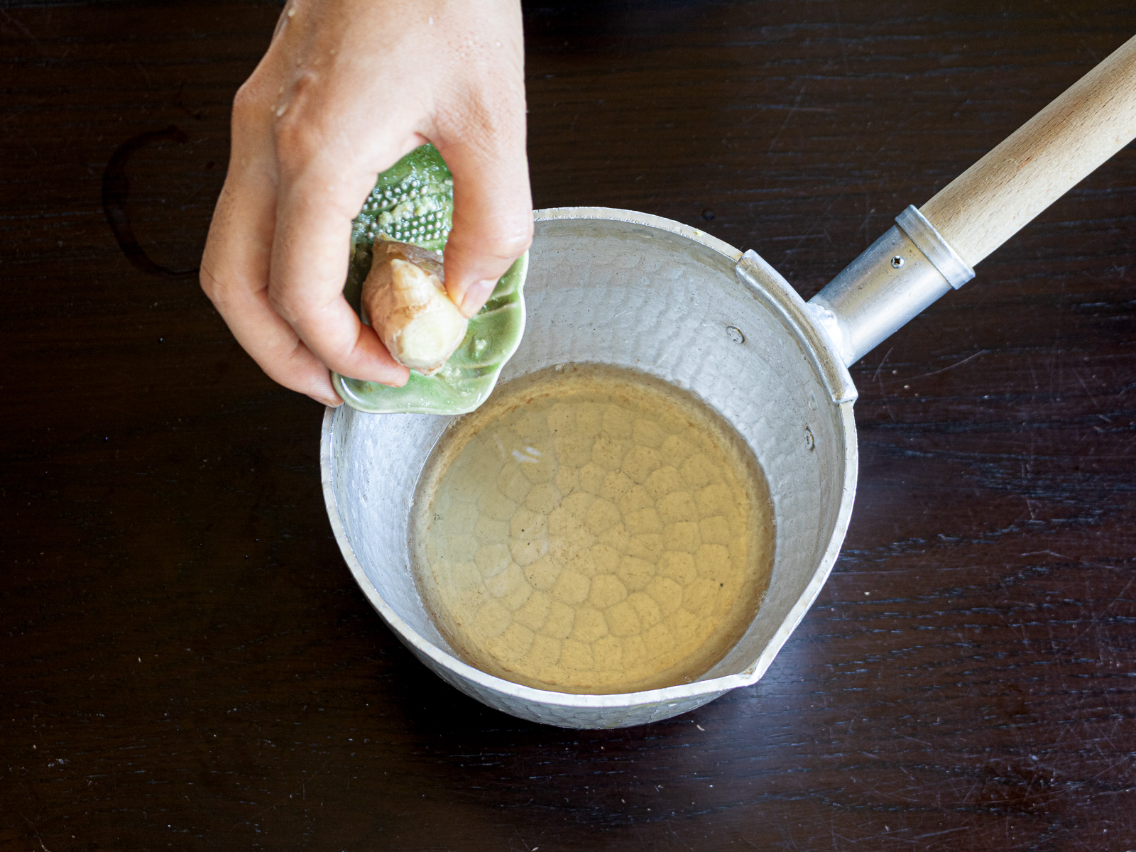 Making ginger syrup in a pot, adding fresh ginger juice. 