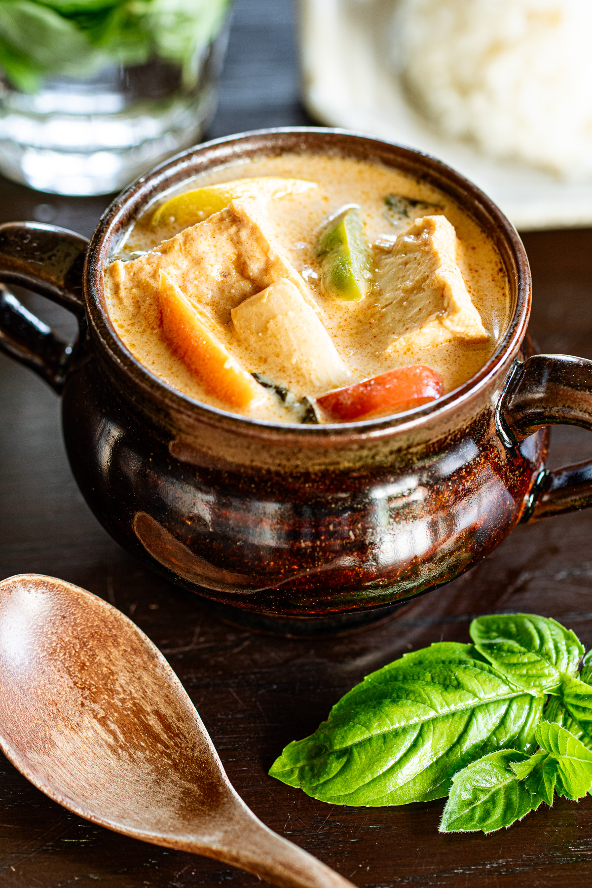素朴な陶器の器に盛られたレッドカレー。夏野菜と厚揚げがごろっと入っていて、白ごはんと一緒に並べられている。