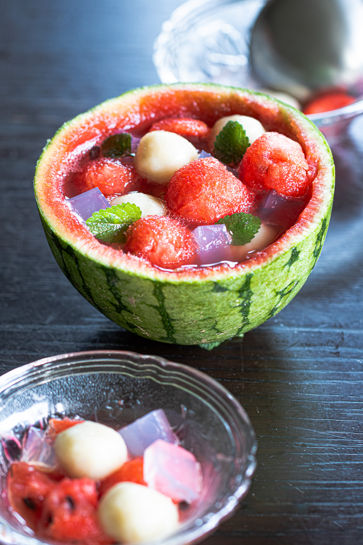 Vegan summer dessert in a watermelon bowl with chewy banana mochi, pale pink agar jelly, and refreshing fruit punch, gluten-free