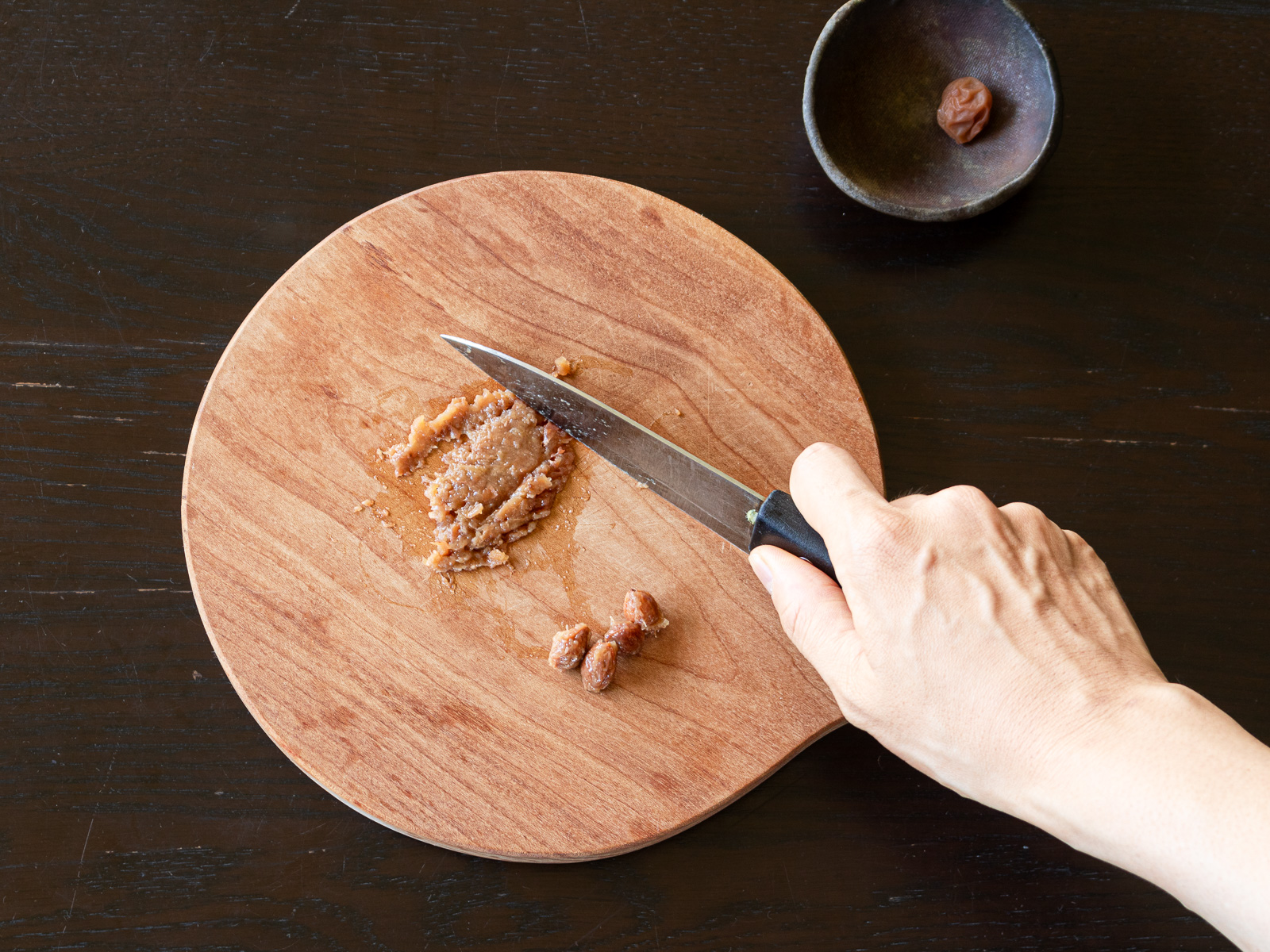 梅干しの種を取り、包丁で叩いてペースト状にする手元の写真。酸味のある梅肉がナスと相性抜群。