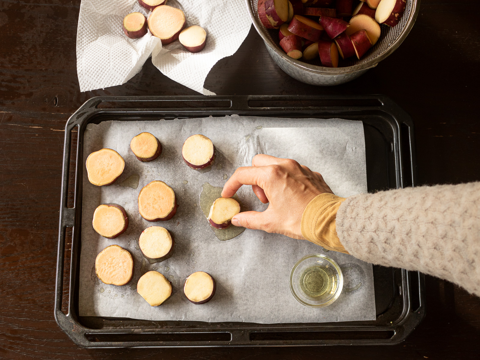 天板にクッキングシートを敷いて、油を垂らし、輪切りにしたサツマイモの表面に油を満遍なくまぶして重ならないように並べる。