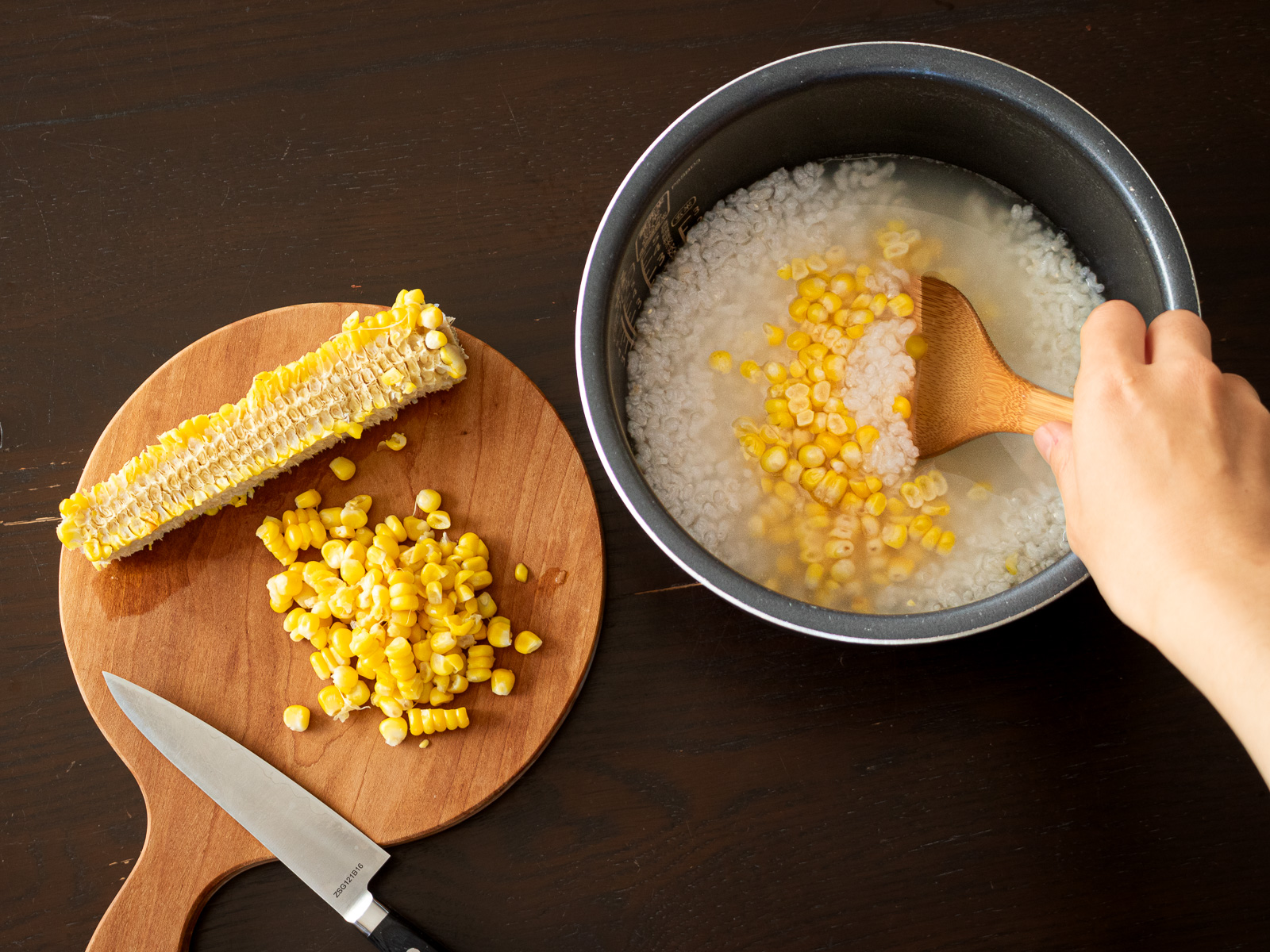 炊いたとうもろこしから包丁で実を削ぎ、削いだとうもろこしの実をお粥に混ぜる