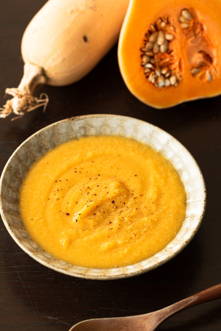 器に盛られたバターナッツかぼちゃとひよこ豆のクリーミーなヴィーガンポタージュスープ、黒胡椒をトッピング