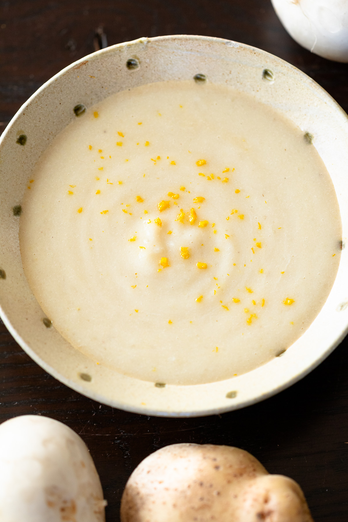 白い器に盛られた、クリーミーなカブと豆乳のヴィーガンポタージュ、ゆずの皮の黄色いすりおろしが浮かぶ