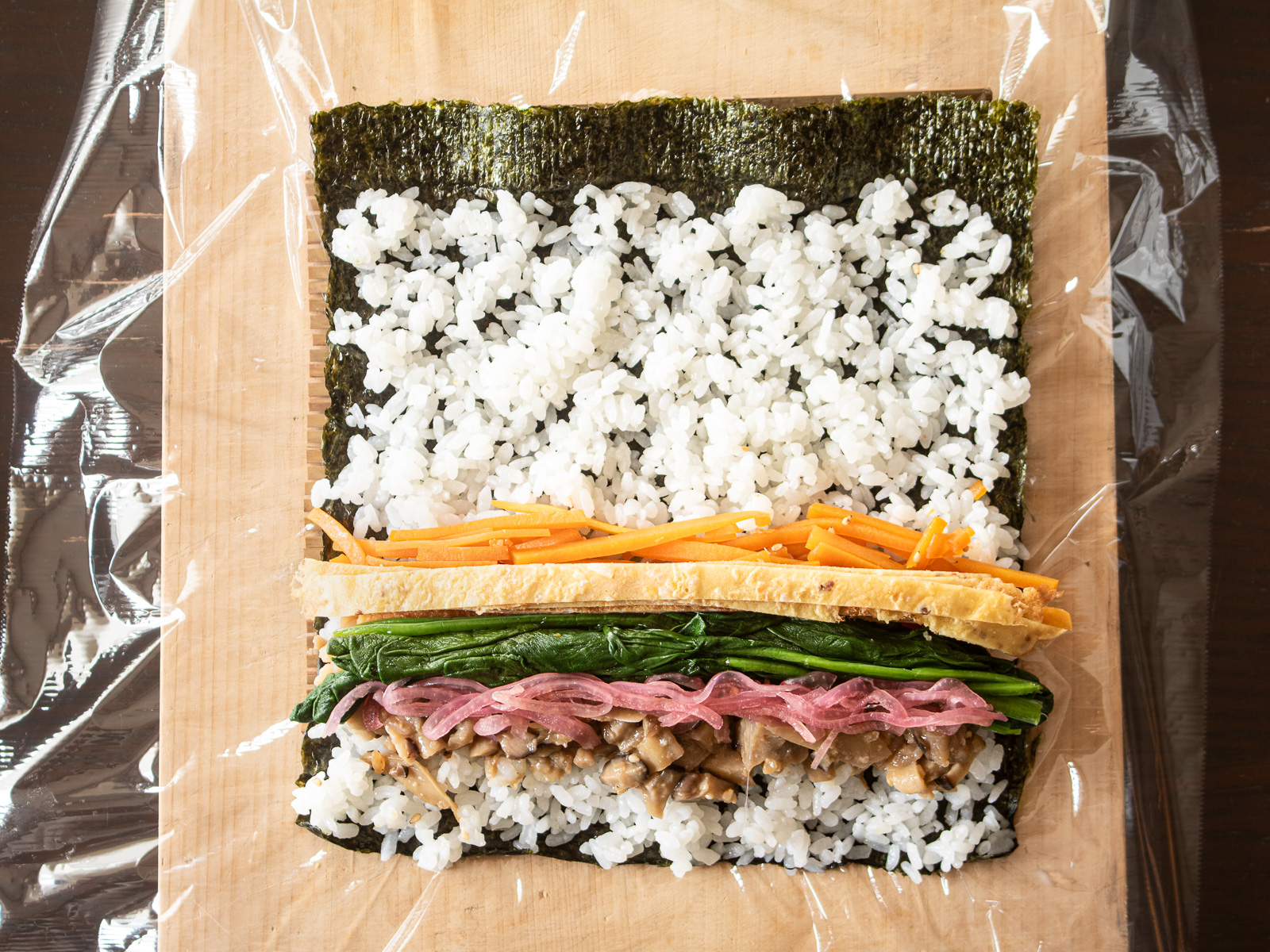 先にのせた具材の上ににほうれん草、玉ねぎの甘酢漬け、ヴィーガン錦糸卵をのせる様子