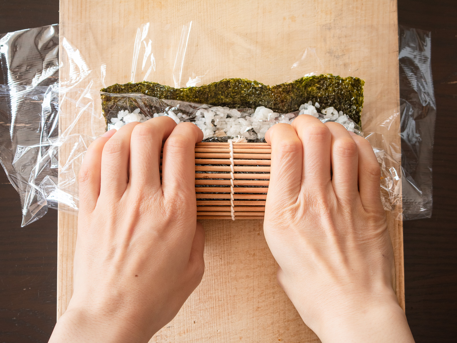 まきすを持ち上げ、具材にかぶせるように太巻きを一度巻く工程