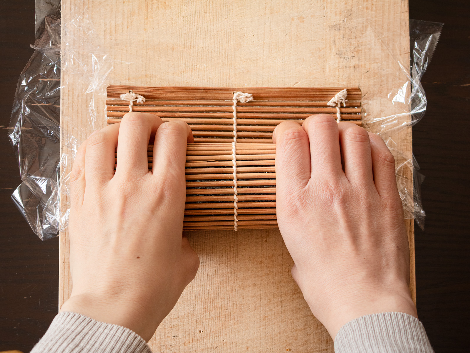 太巻きが巻き終わり、まきすの上から軽く手でおさえ、形を整えているようす