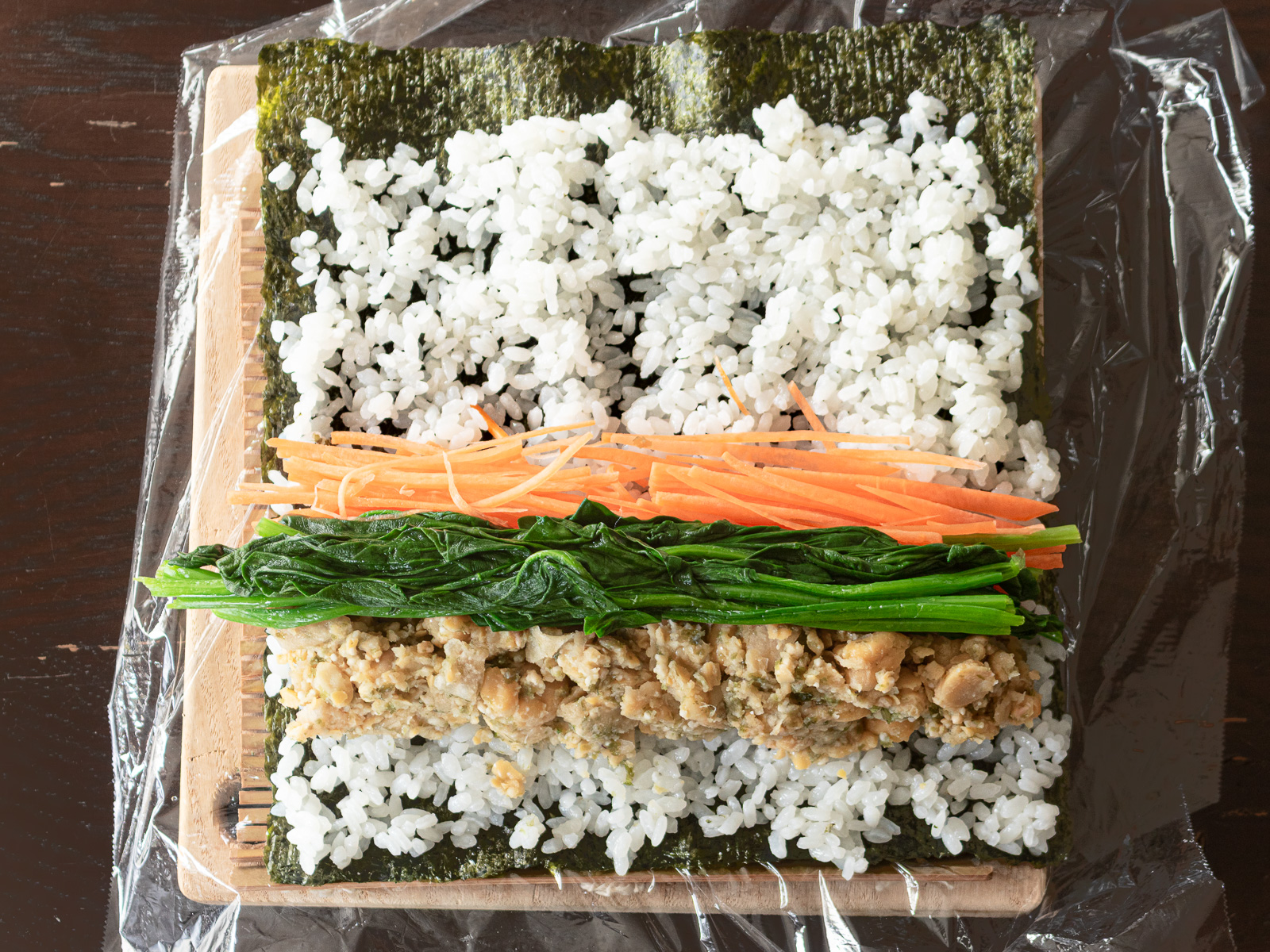 海苔の上に薄く広げたごはんの上に、ヴィーガンツナマヨを手前に、その奥隣に千切りのにんじん、二つの境目の上にほうれん草をのせた、巻く前のヴィーガン海苔巻き寿司