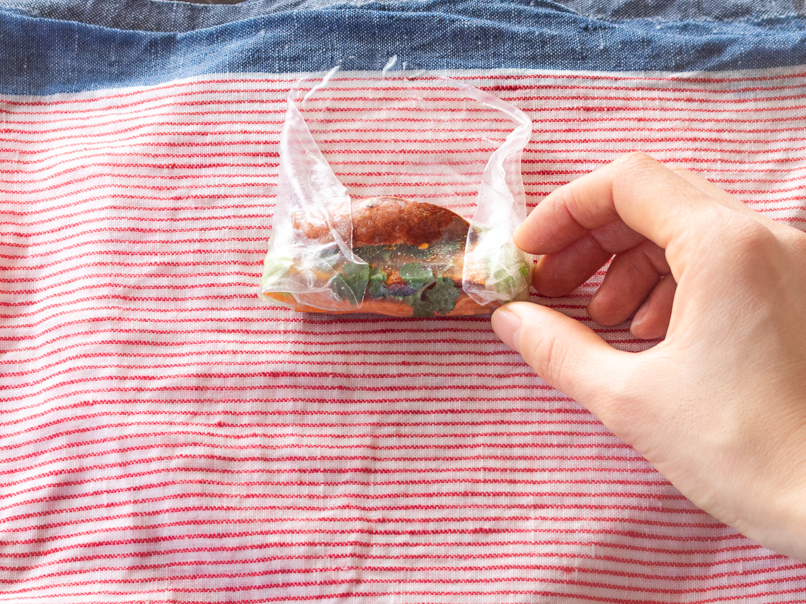 生春巻きの両端を中心に折りたたむ様子。ライスペーパーで破れないように巻くコツを実践