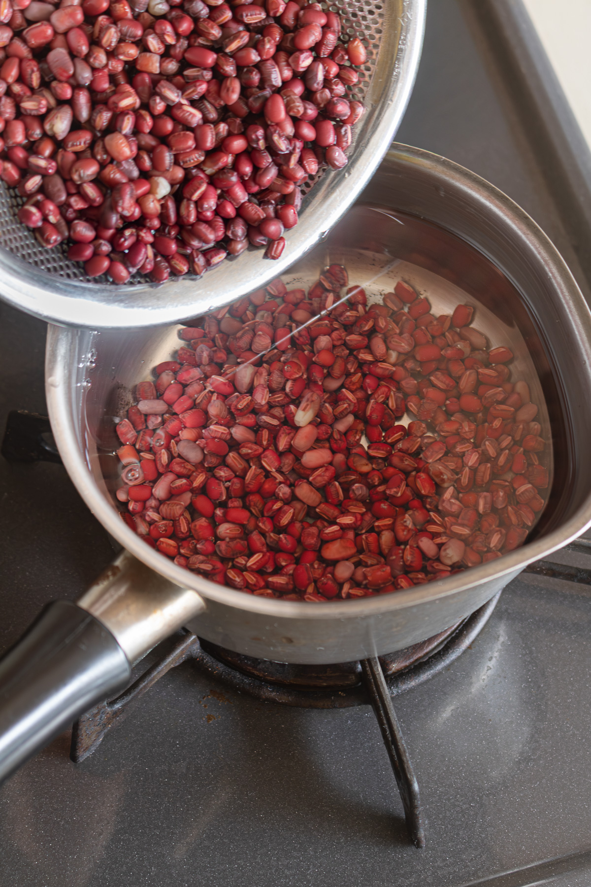 Draining adzuki beans through a sieve for the parboiling step
