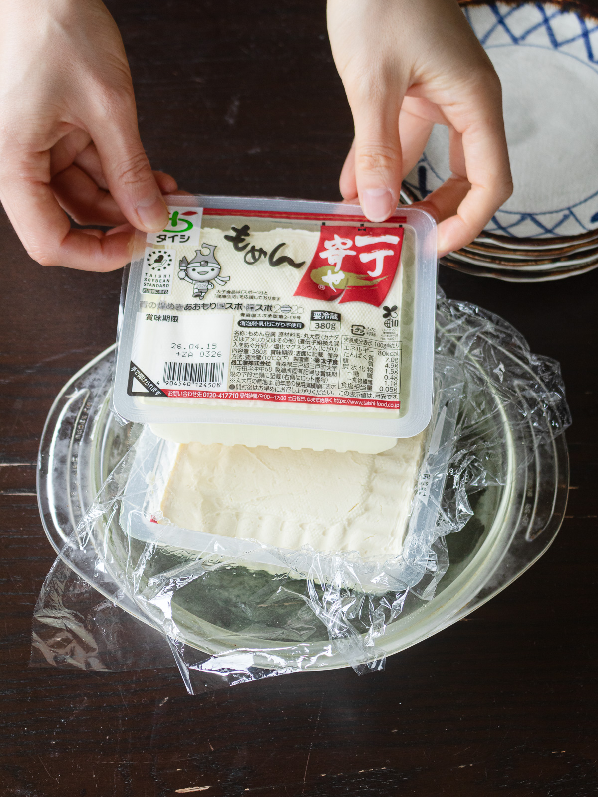 木綿豆腐の水切り方法：パックごと皿にのせてラップと豆腐で重石をする